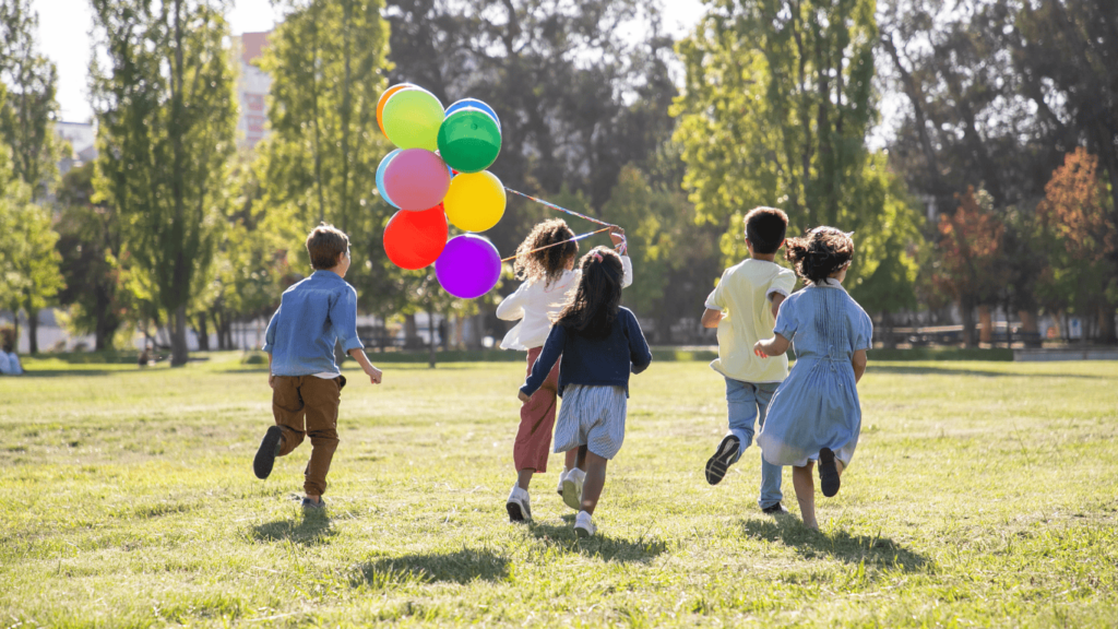 Cinco (5) niños jugando al aire libre con globos
